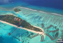 Τα 10 πράγματα που πρέπει να κάνεις όταν επισκεφθείς τις Μαλδίβες Εναέρια λήψη με drone από νησί στις Μαλδίβες με λευκή παραλία, τιρκουάζ νερά και bungalows πάνω στο νερό.