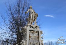 Το άγαλμα του Βόλφγκανγκ Αμαντέους Μότσαρτ στους κήπους του Burggarten στη Βιέννη, με φόντο πράσινο τοπίο και κλασική αρχιτεκτονική.