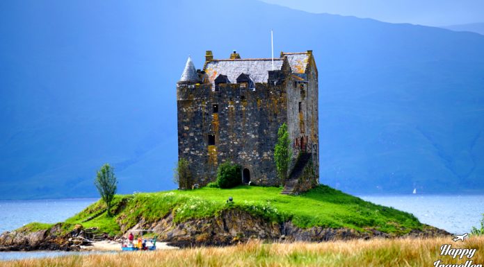 Το Castle Stalker, ένα επιβλητικό μεσαιωνικό κάστρο χτισμένο σε νησάκι μέσα σε λίμνη στη Σκωτία, με καταπράσινο τοπίο γύρω του.
