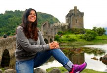 Η Ηλέκτρα ποζάρει μπροστά από το ιστορικό Eilean Donan Castle στη Σκωτία, με τα βουνά και τη λίμνη στο φόντο.