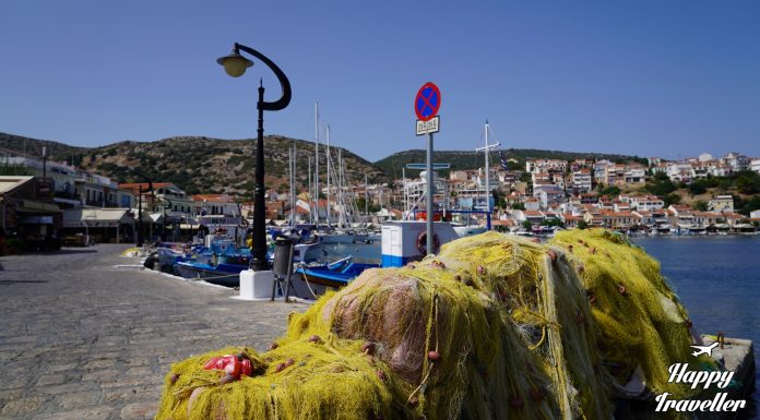 Πανοραμική εικόνα του λιμανιού του Πυθαγορείου στη Σάμο, με πολύχρωμα καΐκια και παραδοσιακά σπίτια στο βάθος.