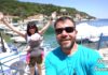 Happy Traveller στην Ιθάκη | Επεισόδιο Ηλέκτρα και Ευτύχης χαμογελούν μπροστά από το γαλήνιο τοπίο της Ιθάκης, με φόντο τη θάλασσα και τα παραδοσιακά σπίτια και τη θαλασσα.