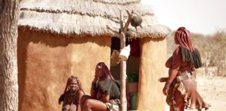 Γυναίκες σε χωριό Himba που κάθονται έξω από την καλύβα τους