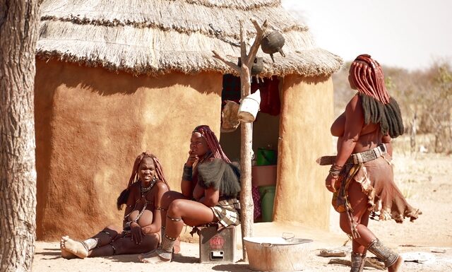 Γυναίκες σε χωριό Himba που κάθονται έξω από την καλύβα τους