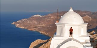 υτύχης στέκεται πάνω σε εκκλησία στην Ανάφη με φόντο τη θάλασσα.