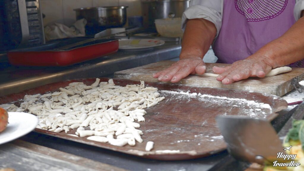 Χέρια γυναίκας από την Κάρπαθο που πλάθει παραδοσιακές μακαρούνες σε ξύλινο πάγκο.