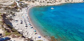 Καταγάλανη παραλία με χρυσή αμμουδιά και βραχώδη τοπία στην Κάρπαθο, κάτω από λαμπερό ήλιο.
