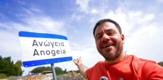 Ευτύχης Μπλέτσας ποζάρει χαμογελαστός μπροστά σε πινακίδα που γράφει «Ανώγεια».