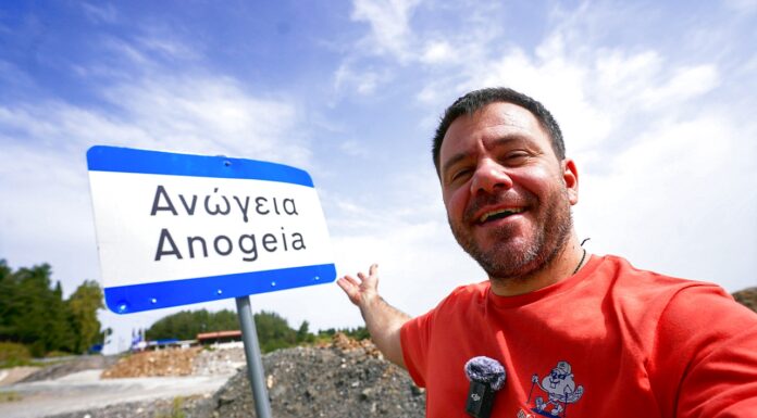 Ευτύχης Μπλέτσας ποζάρει χαμογελαστός μπροστά σε πινακίδα που γράφει «Ανώγεια».