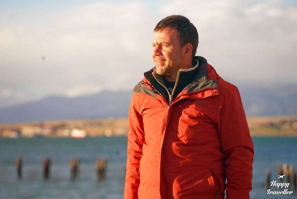 Ευτύχης Μπλέτσας στον παλιό μώλο του Puerto Natales στη Χιλή, πάνω στην ξύλινη προβλήτα του ιστορικού λιμανιού με φόντο το φιόρδ Última Esperanza και τα βουνά της Παταγονίας