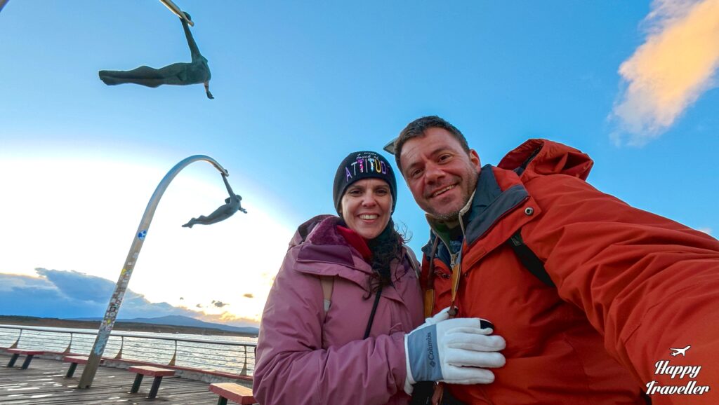 Ευτύχης Μπλέτσας και Ηλέκτρα Αστέρη στο Monumento al Viento στο Puerto Natales, ποζάρουν μπροστά από το εμβληματικό γλυπτό που συμβολίζει τους ισχυρούς ανέμους της Παταγονίας, με φόντο το παραλιακό μέτωπο και το φιόρδ Última Esperanza