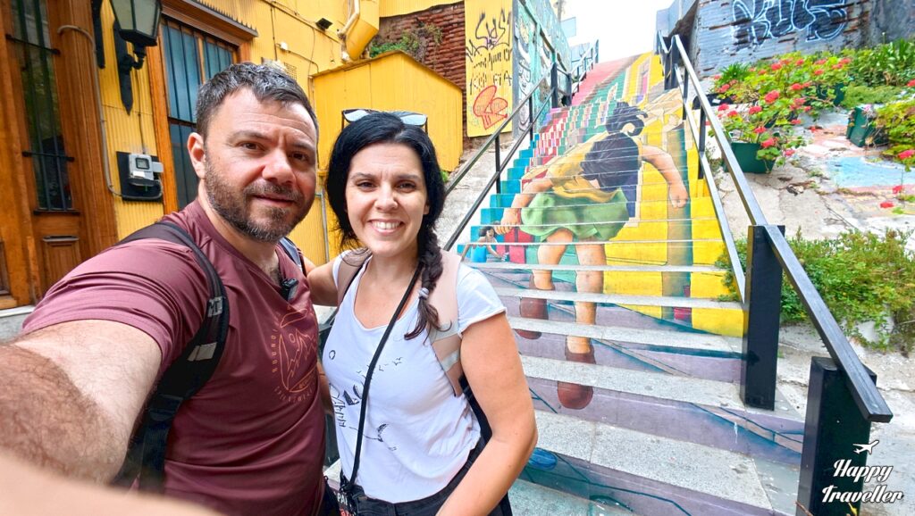 Ο Ευτύχης Μπλέτσας και η Ηλέκτρα Αστέρη στο Βαλπαραΐσο της Χιλής μπροστά σε πολύχρωμο γκράφιτι ζωγραφισμένο πάνω σε σκαλιά.